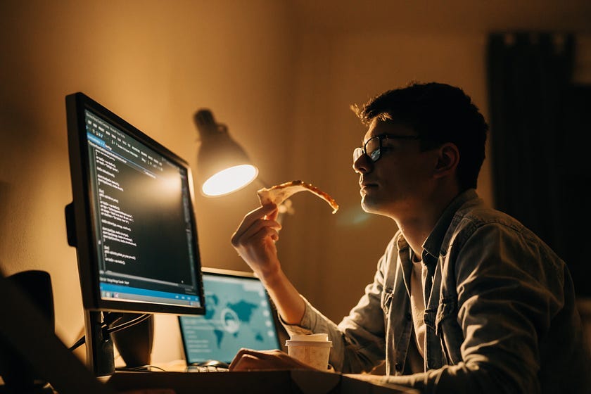 Young programmer eating pizza while working late night in his home