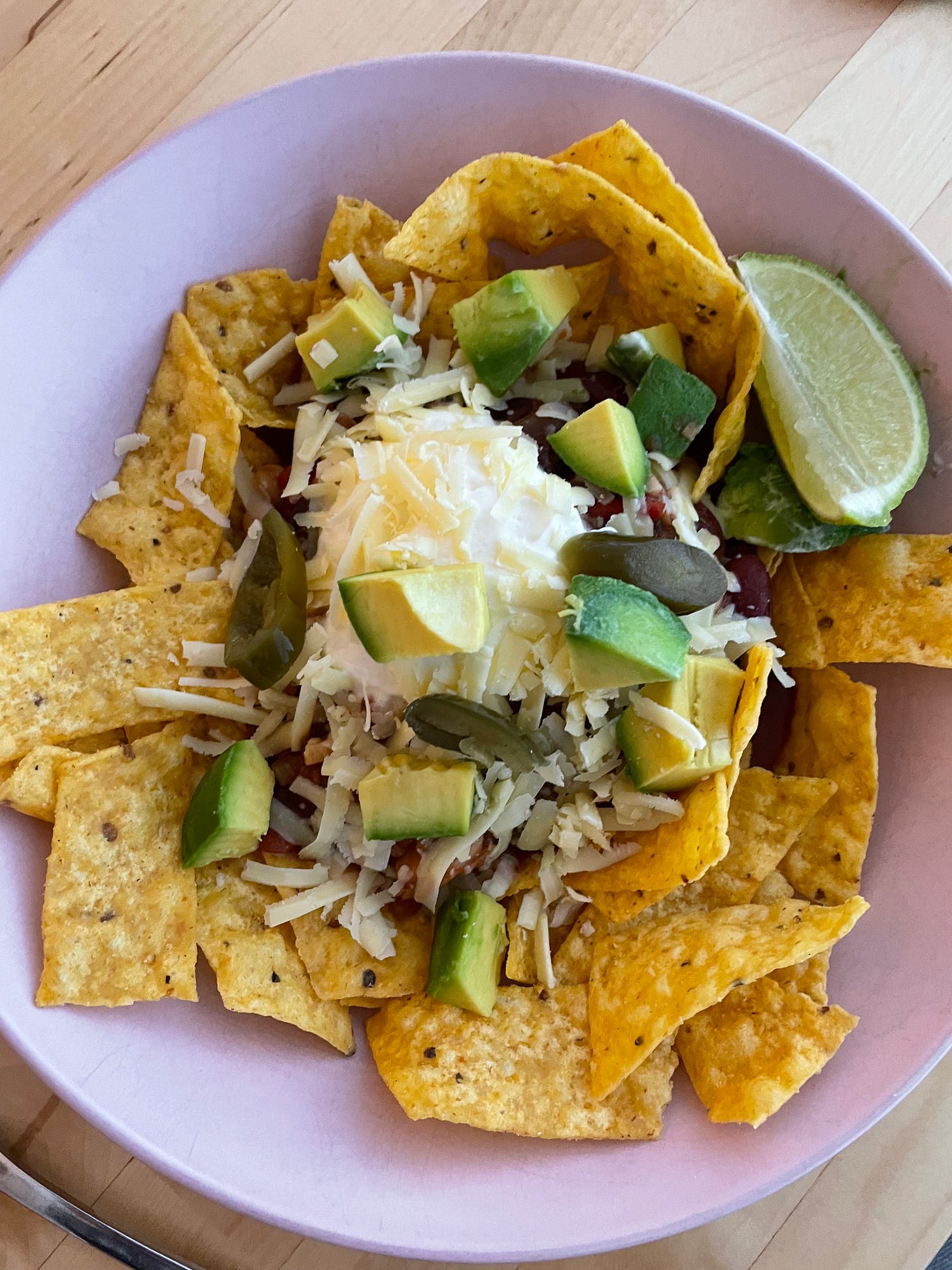 Bowl of nachos topped with vegetarian chilli, sour cream, avocado, pickled japalenos and cheddar cheese.