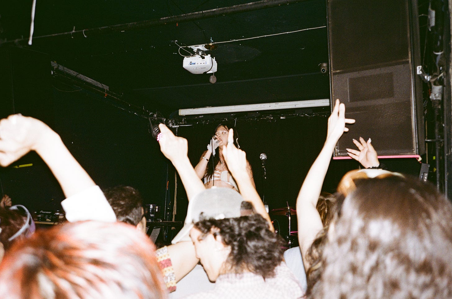 In a 35mm film photo, Princess Xixi raps onstage to an out-of-focus crowd, who throws their hands up
