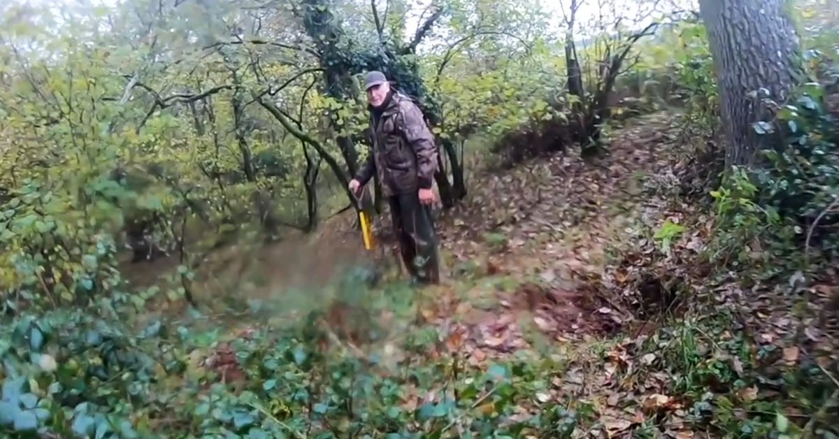 A man stares at the camera holding a spade next to a badger sett entrance