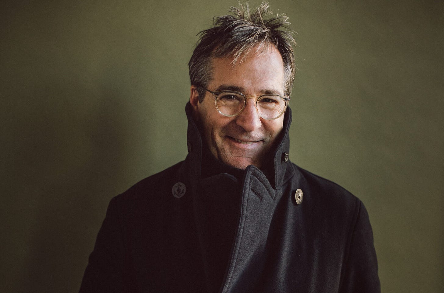 Richard Shindell smiling at the camera in an overcoat and glasses