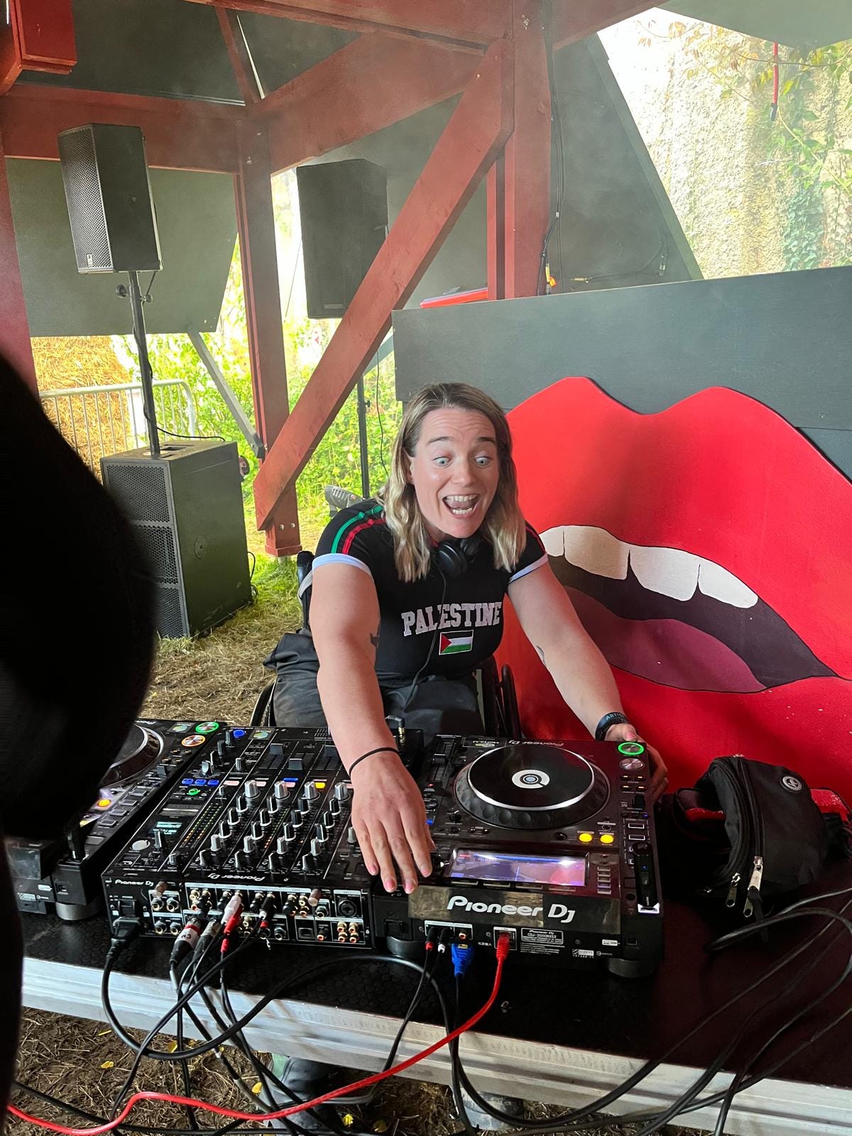 I am DJing. As I reach for the decks, my eyes are wide and I am in the middle of singing a song very passionately.  I am wearing a Palestine tee, almost like a football shirt, and the speakers are hanging behind me. 