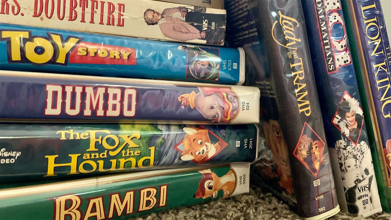 A collection of classic VHS tapes in their original plastic containers. On the spines we see the names Bambi, the Fox and the Hound, Dumbo, Toy Story, Mrs. Doubtfire, Lady and the Tramp, 101 Dalmations, and The Lion King.