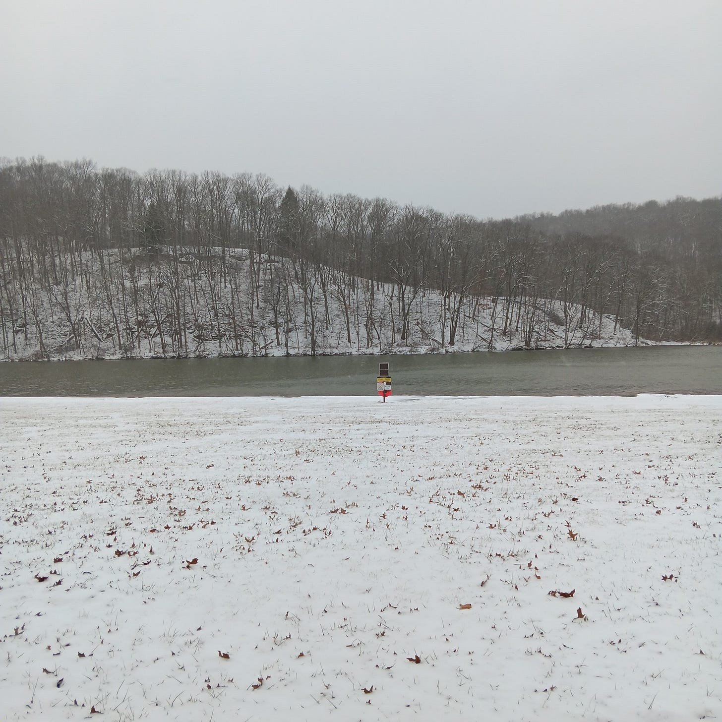 A wide shot of the beautiful lake, all gray and white in wintertime with bare trees on the far shore. 