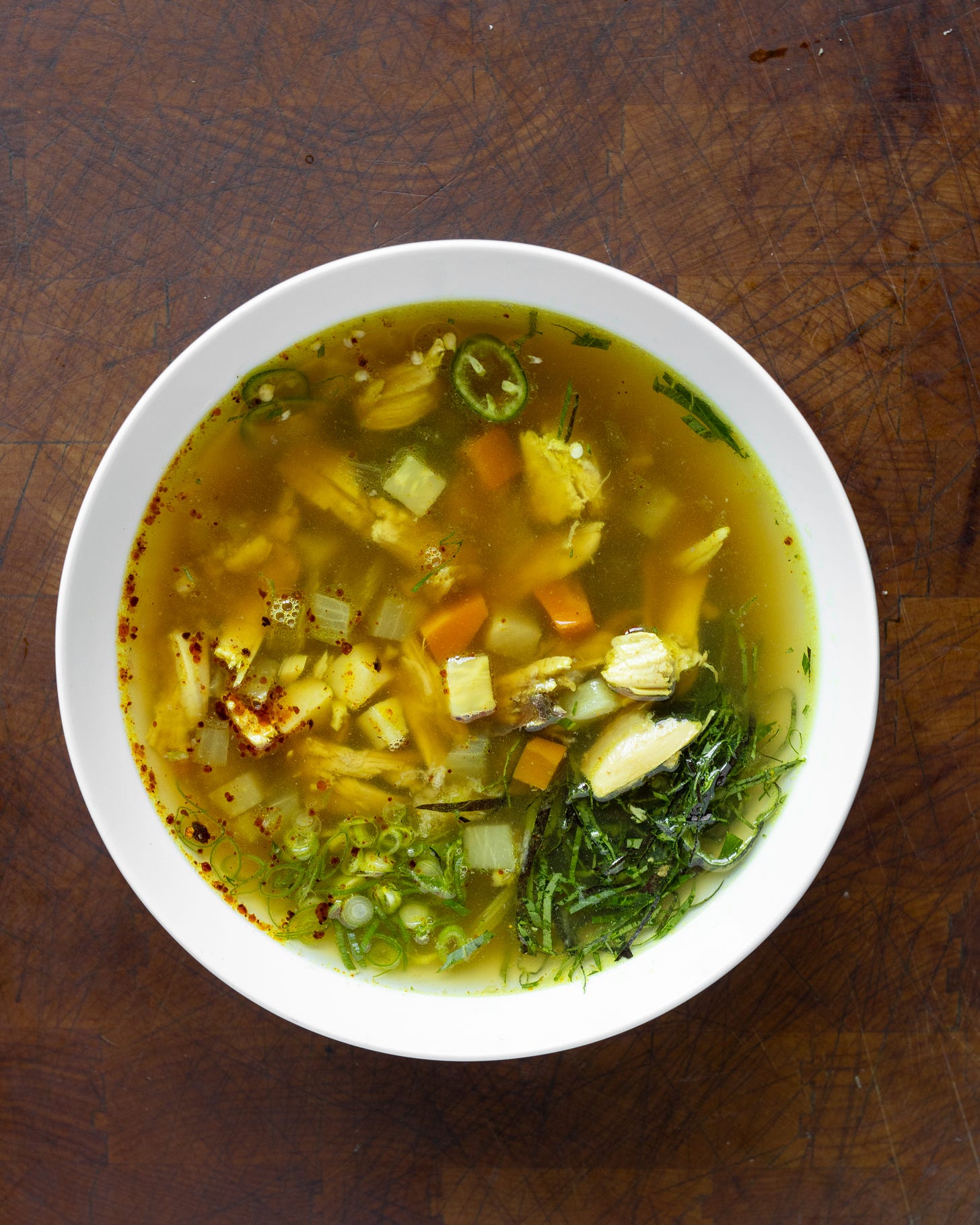 Overhead photo of a bowl of chicken soup showing some chopped herbs and green onion floating on top
