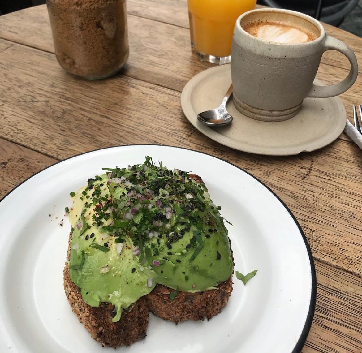 A beautiful avocado toast on a wooden table with a cappuccino by its side