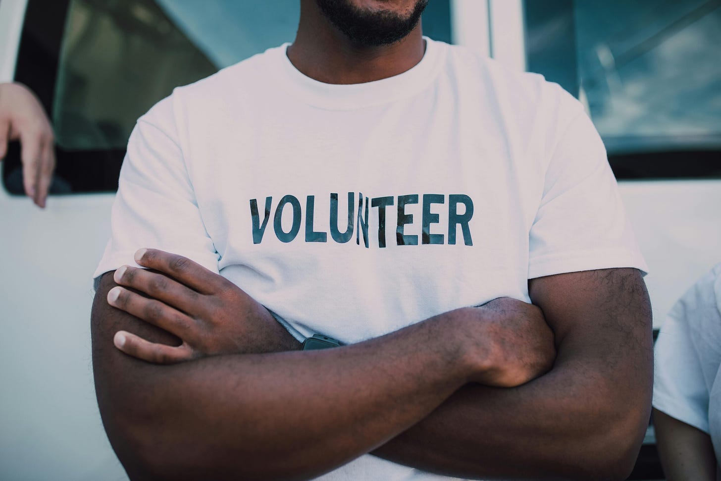 Man standing with arms crosses, wearing a t-shirt that reads 'volunteer'