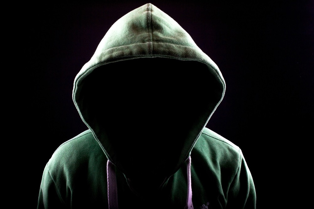 an anonymous figure in a hooded top, lurking in the dark