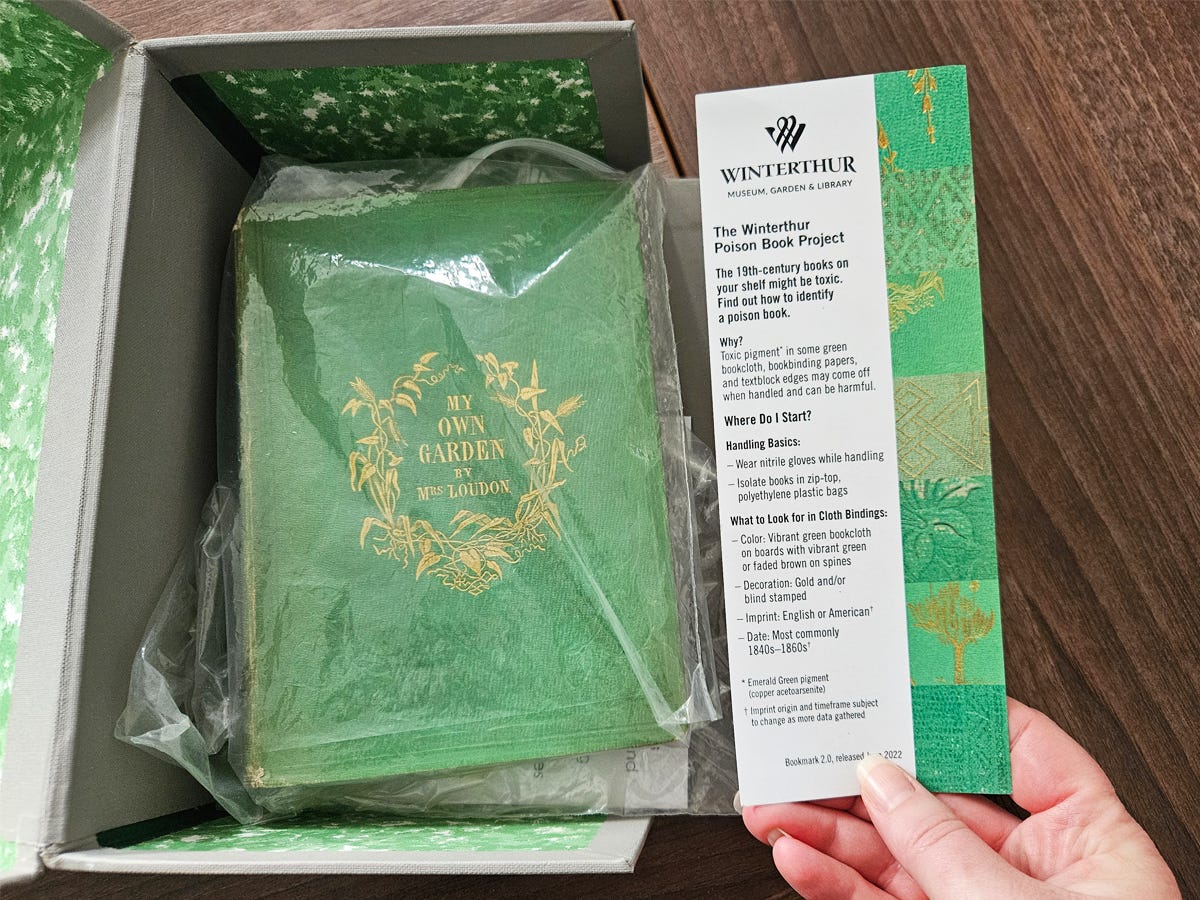 A book in a plastic bag inside an open box, with a hand holding a bookmark next to it