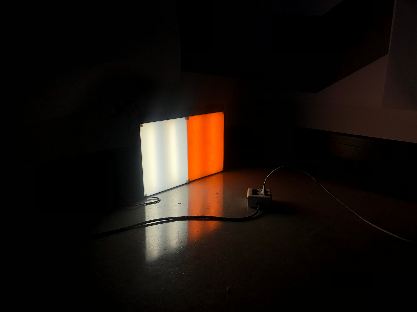 An image depicts two light boxes side by side in a dark room. The leftmost light is cool and white. The rightmost light is orange and warm.