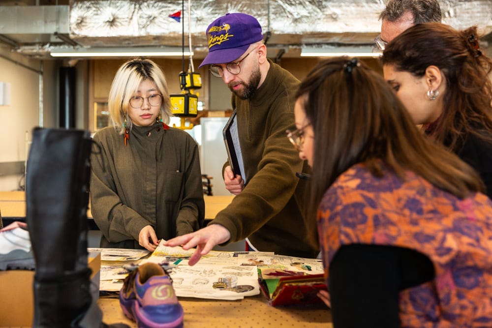 Group of people in a classroom looking at shoe prototypes and drawings.