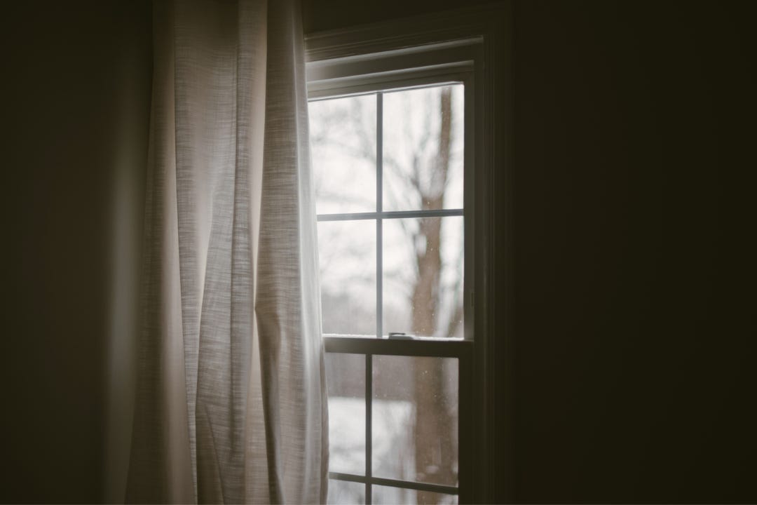 Window with white curtain, snow falling outside