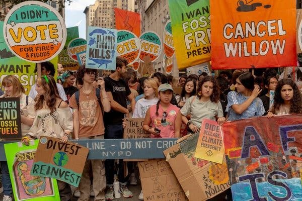 A crowd of young people in a city street, holding signs with slogans like “I didn’t vote for fires and floods” and “Biden, declare a climate emergency.”