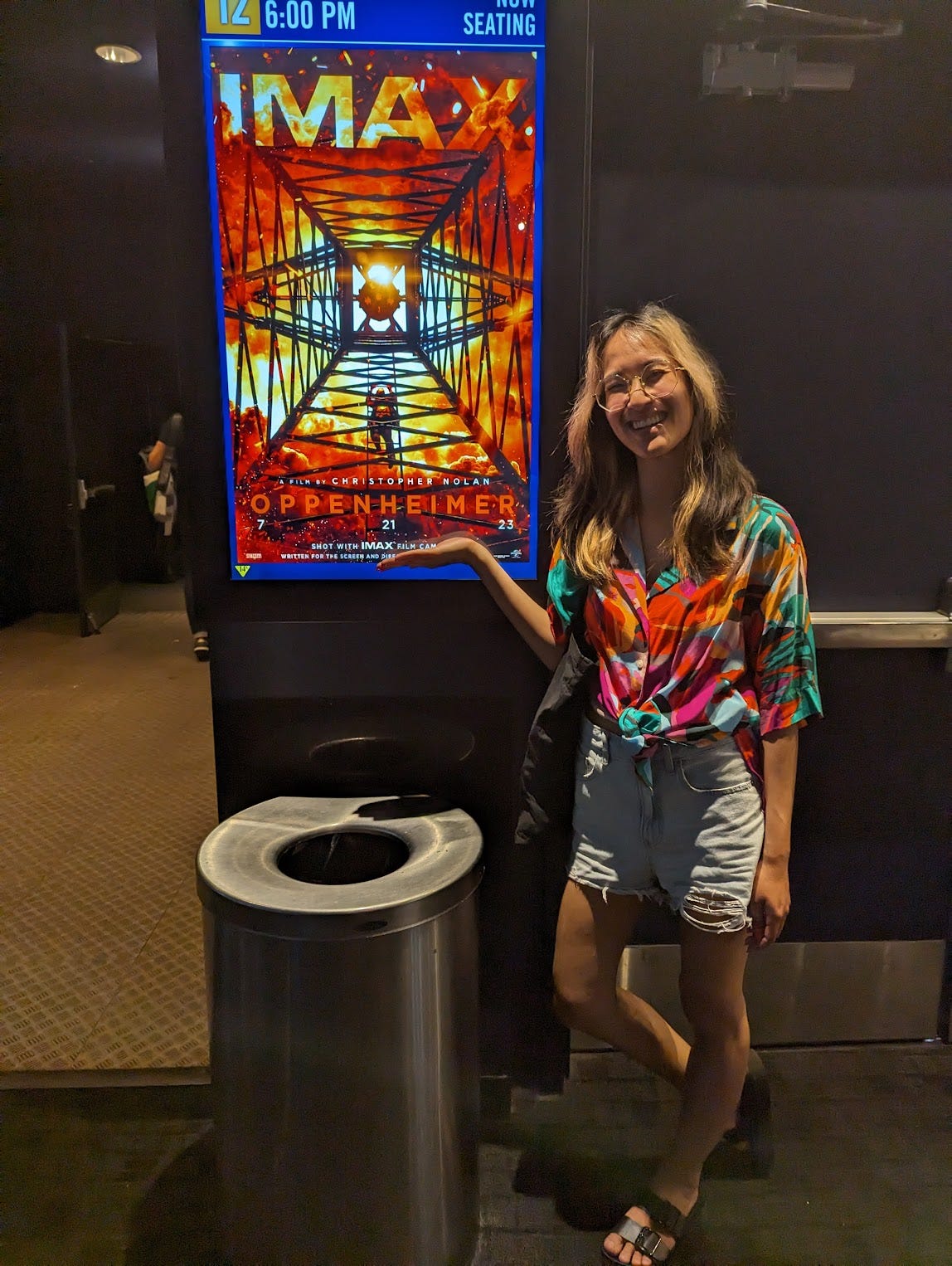 Sennah poses with the Oppenheimer poster with a trash can in front of it