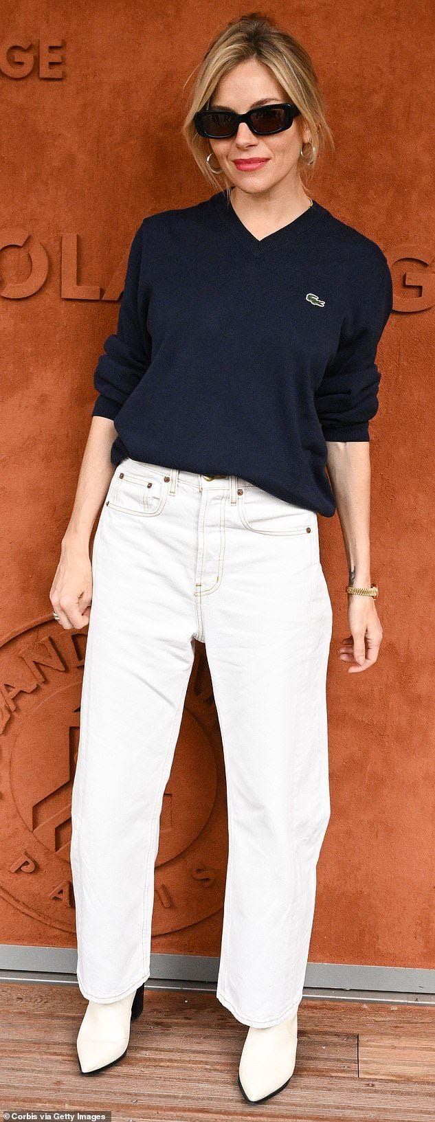 This may contain: a woman standing in front of a wall wearing white pants and black sweater with sunglasses on her head