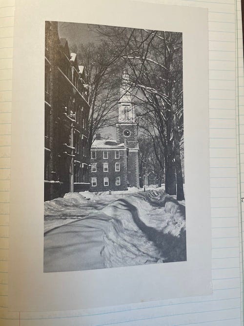 Black and white photo of paths through deep snow on a college campus with a dormitory and a 3-story chapel with a bell tower.