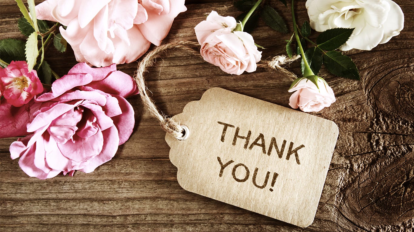  archival tag with the words "thank you" attached with a rope and sitting on a wooden table with pink and red roses
