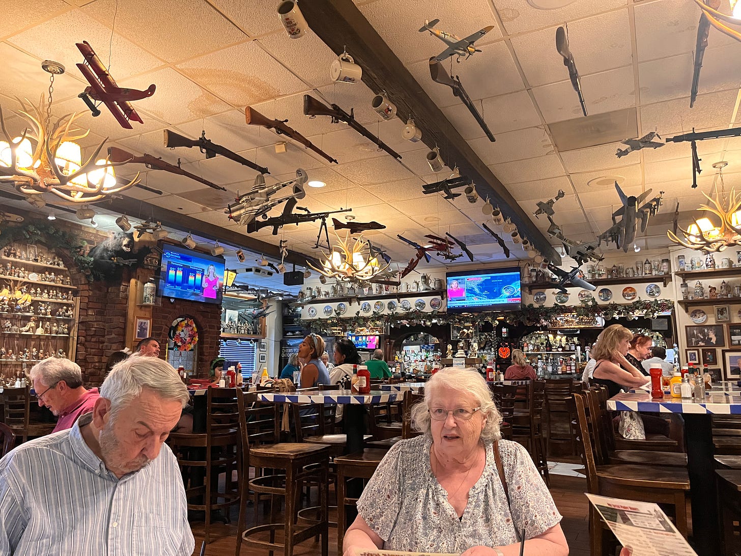 Kitsch filled overwhelming view of German restaurant with my parents at a table and all manner of guns hanging from the ceiling