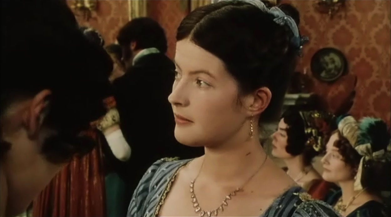 Charlotte Lucas is talking to Lizzy and looking at Mr. Darcy glancing at Lizzy.