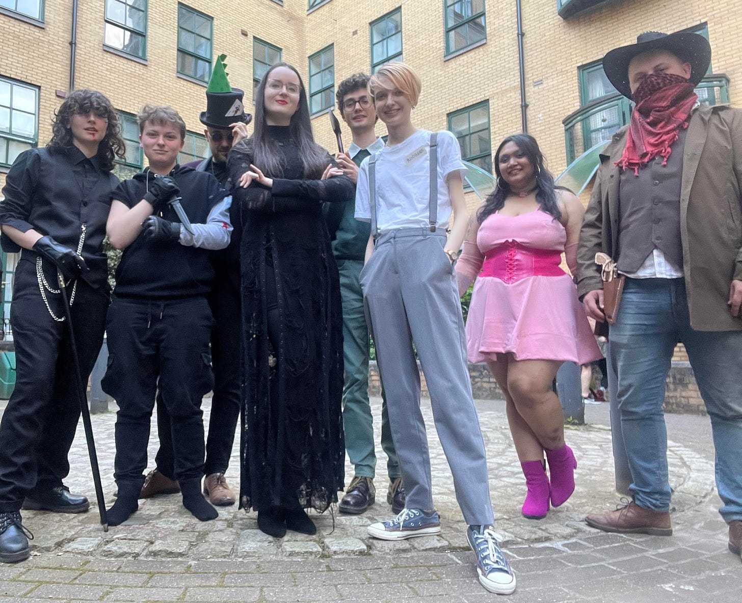 Photograph of eight people wearing costumes of various efforts. There is Lucien Malfoy, Bucky Barnes, The Mad Hatter, Morticia Adams, The Green Knight from the Legend of King Arthur, a pre-serum Steve Rodgers, a Winx club fairy and a generic cowboy who is happy to be the lone ranger or cowboy beebop you decide. ,