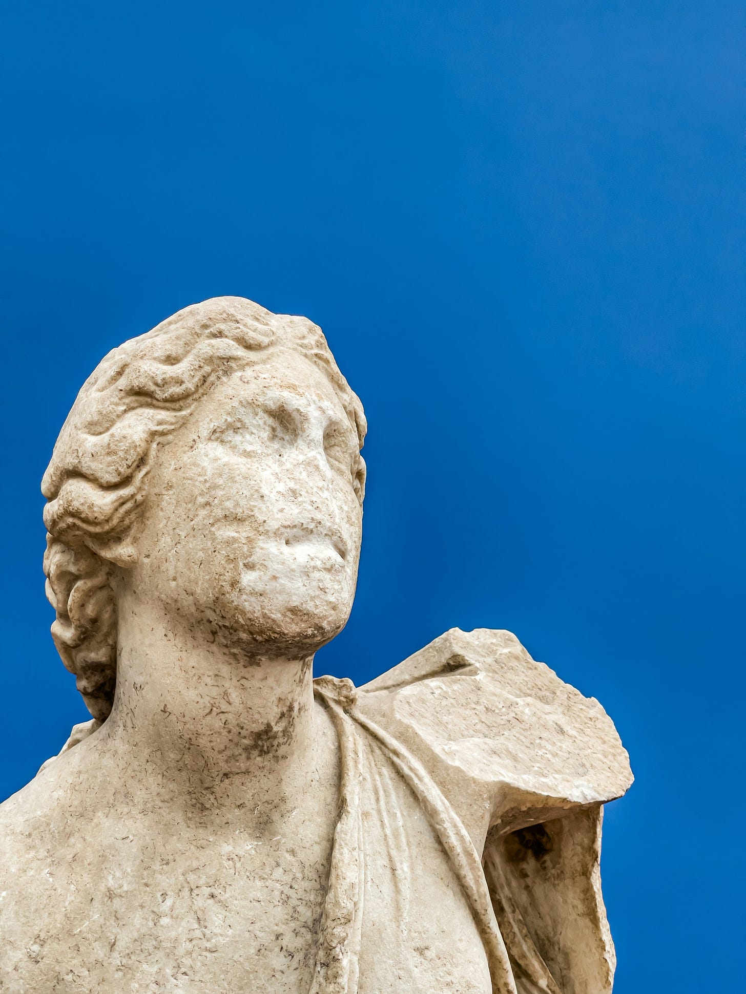 Photo of broken and worn stone or marble statue against a blue background.