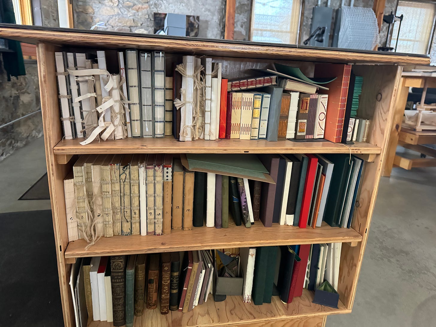 A wooden bookshelf filled with books. The books have spines of various kinds and are used as references for bookbinders to look at while they practice.