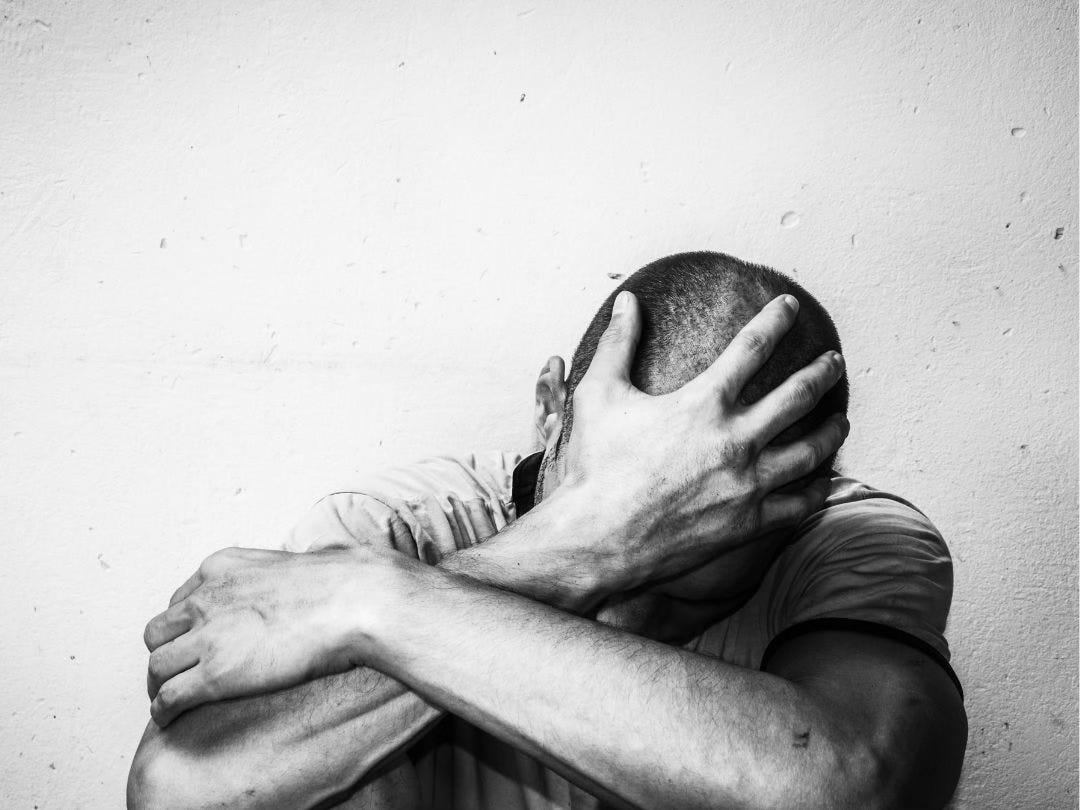 Black and white photo of a man in deep grief, his arms crossed with a hand covering his face.