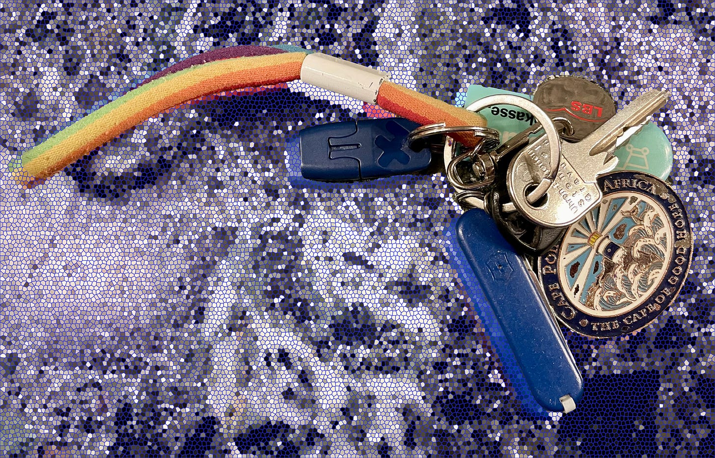  A reduced set of keys on a mosaic-textured surface, including a rainbow fabric loop, a blue Swiss Army knife, a Cape Point-South Africa medallion, and a few house keys.