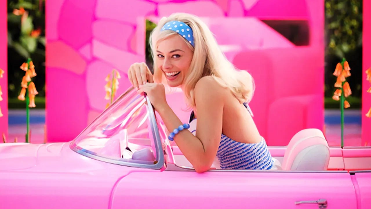 Margot Robbie as Barbie, smiling, sitting in a pink car