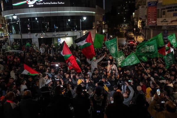 A large crowd of people in a street, many waving Palestinian flags and green Hamas flags with Arabic script on them.