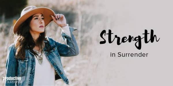 A woman with long, dark hair in a wide-brimmed hat stares across the field, holding the brim of her hat. Text Overlay: Strength is Surrender.