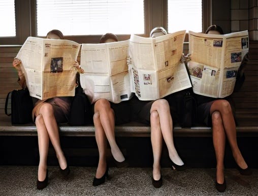 Four women sitting side by side on a bench, all holding up newspapers that completely cover their faces. The image captures a playful, yet reflective, moment of people immersed in catching up with the news. Their identical positioning emphasizes the importance of staying informed in today’s fast-paced world.