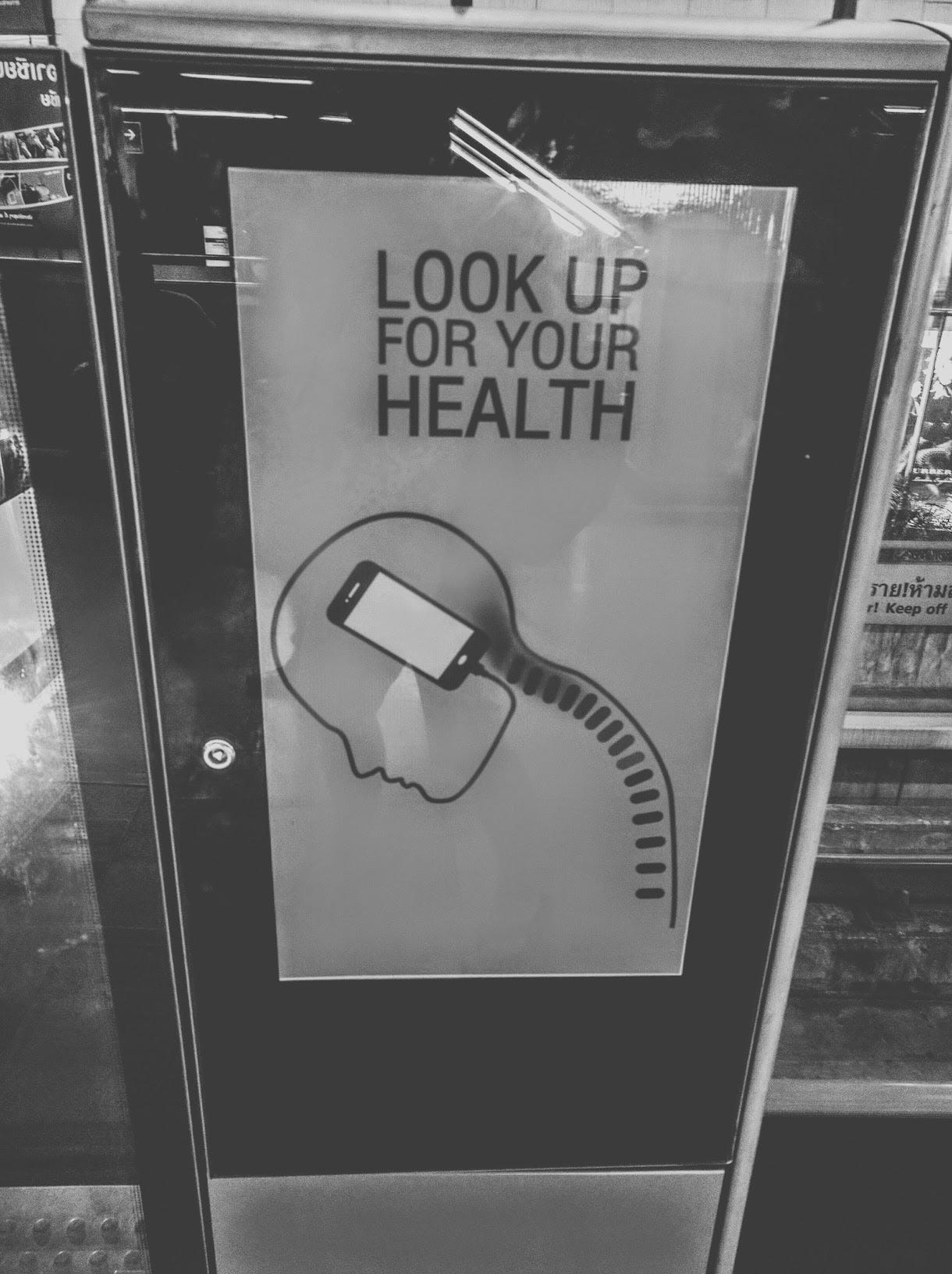 A poster at a subway station says "Look up for your health," and show an illustration of a skeleton curled over a phone that winds into the skull