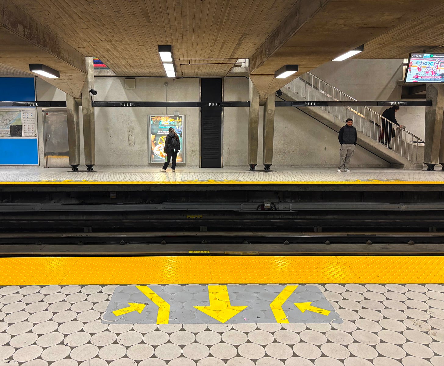 subway station in montreal showing yellow arrows pointing in both directions to direct passengers - two people stand across the platform