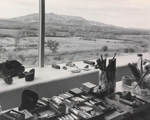 A black-and-white photograph of paints, brushes, and other art supplies on a wide windowsill that overlooks a mountain landscape. A black-and-white photograph of paints, brushes, and other art supplies on a wide windowsill that overlooks a mountain landscape.