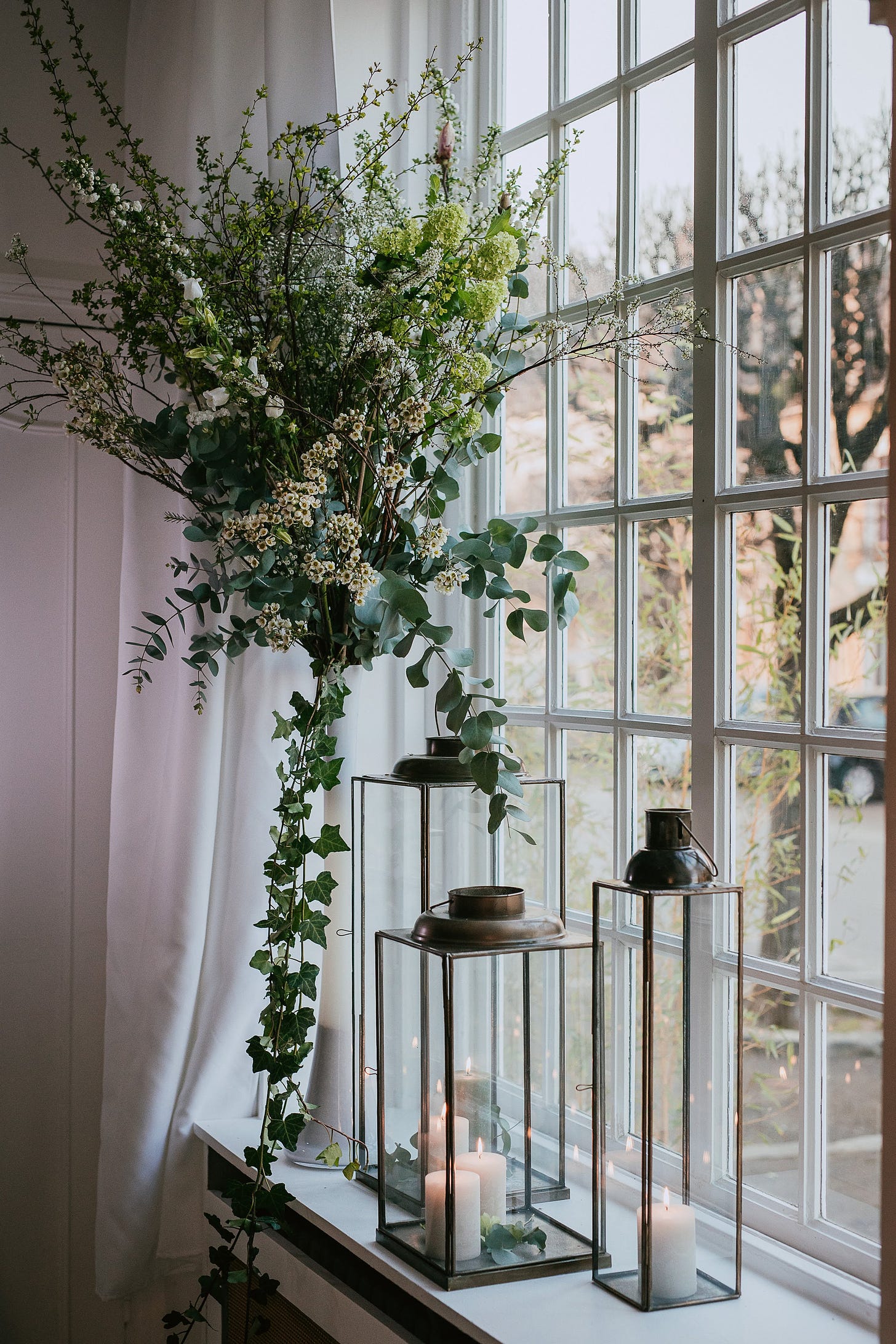 Branches, blossoms and candle lanterns decorate a window at a wedding