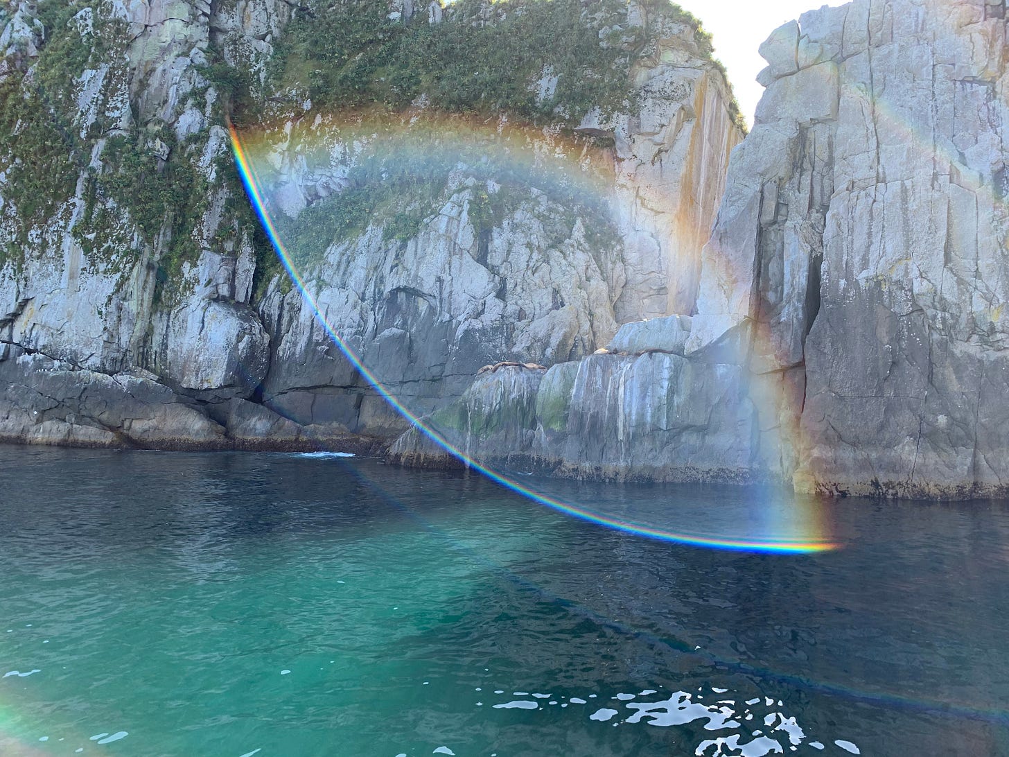A rainbow (the symbol for the LGBTQ community since 1978, over turquoise water