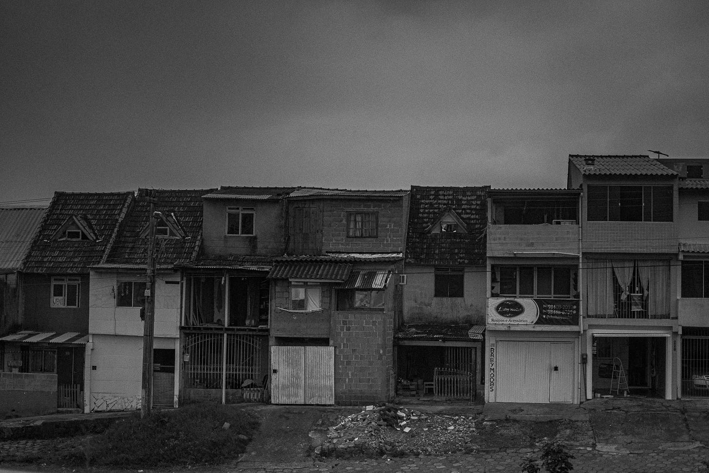 Fotografia em preto e branco de diversas casas coladas, uma ao lado da outra, em uma comunidade pobre na Grande Florianópolis. 