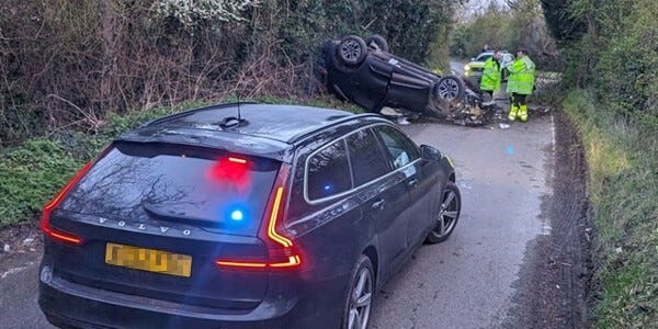 Blue volvo car held while officers del with an overturned car further up the road