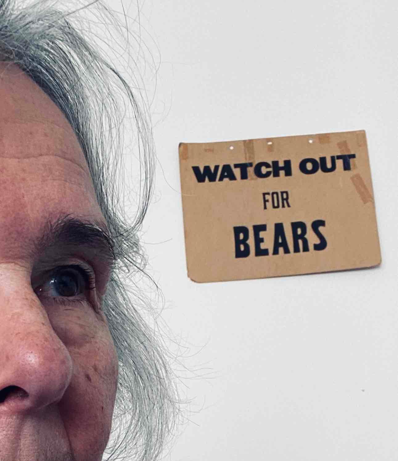 Older woman's face and messy hair, beside a sign reading "Watch out for BEARS"