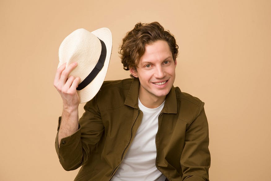 Man holding straw hat, brown shirt over white T-shirt, smiling