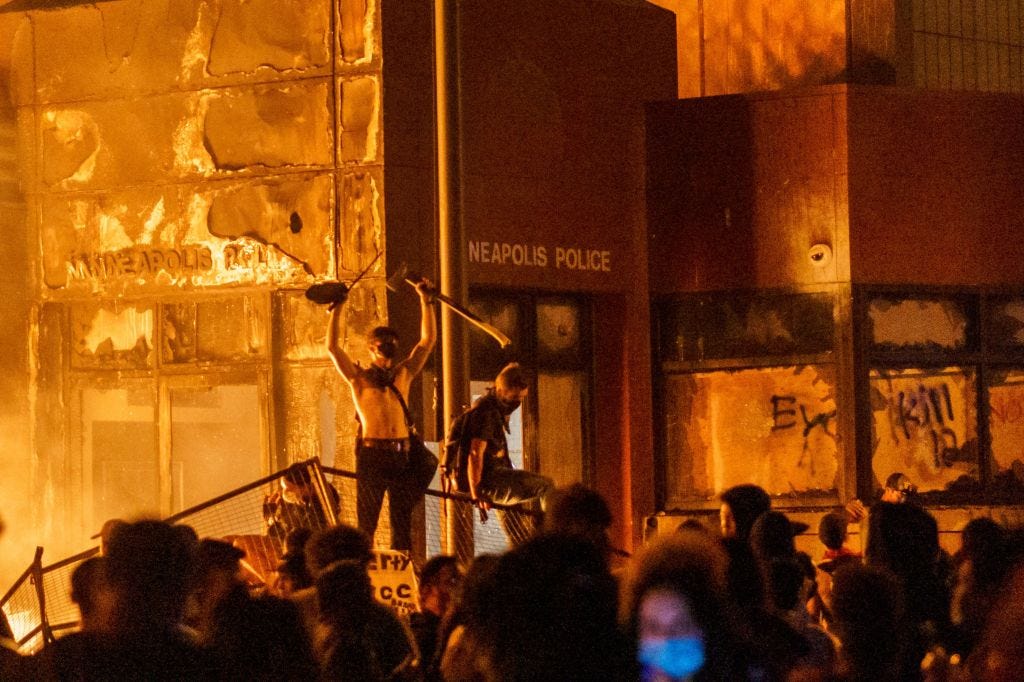 Flames from a nearby fire illuminate protesters standing on a barricade in front of the Third Police Precinct on May 28, 2020 in Minneapolis, Minnesota, during a protest over the death of George Floyd