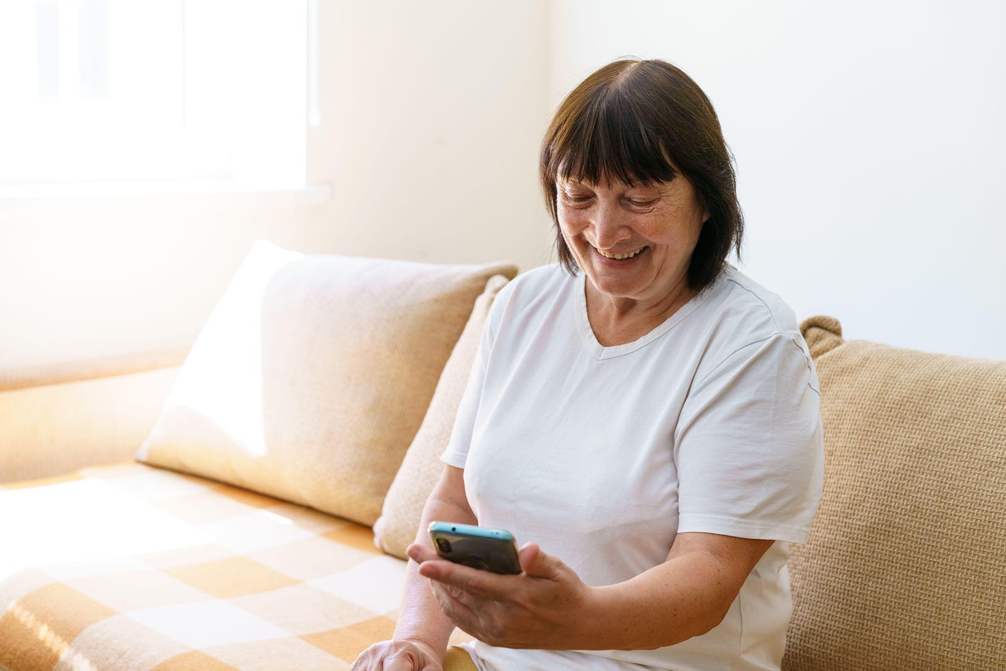 Middle aged woman sat on a sofa smiling at her phone 