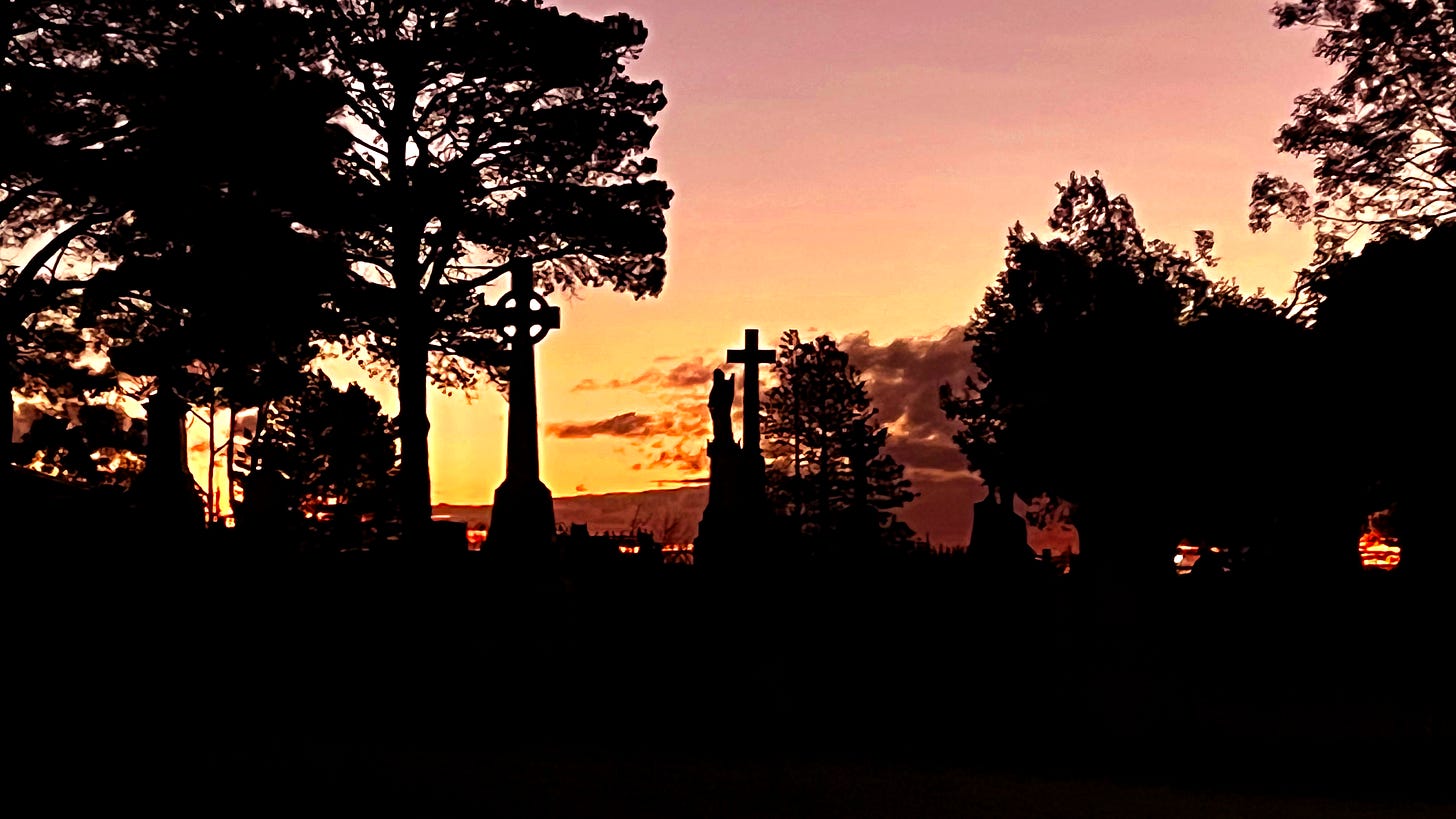 Tall cross grave markers silhouetted by a sunset.