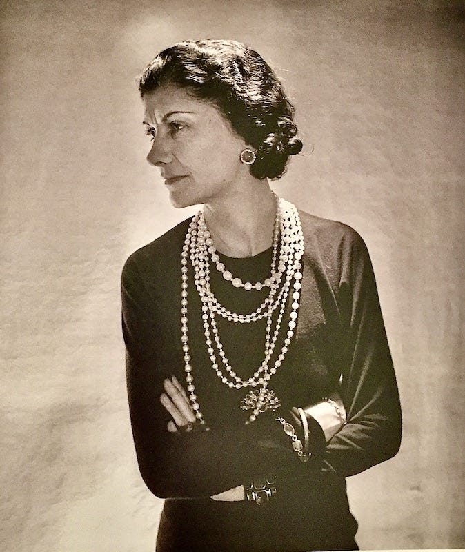 Black and white photograph of Coco Chanel wearing a lot of different sized pearls around her neck.