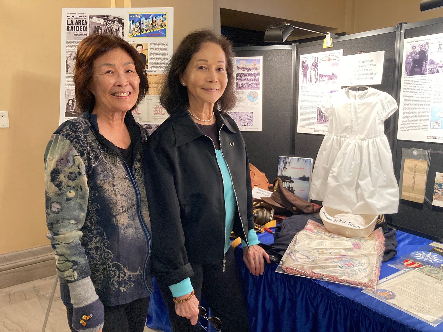 Cindy Yee (left) with Nancy Kwan at the AAPI History Month Exhibit with the little white dress made of parachute cloth. Photo Montgomery Hom, All Rights Reserved.