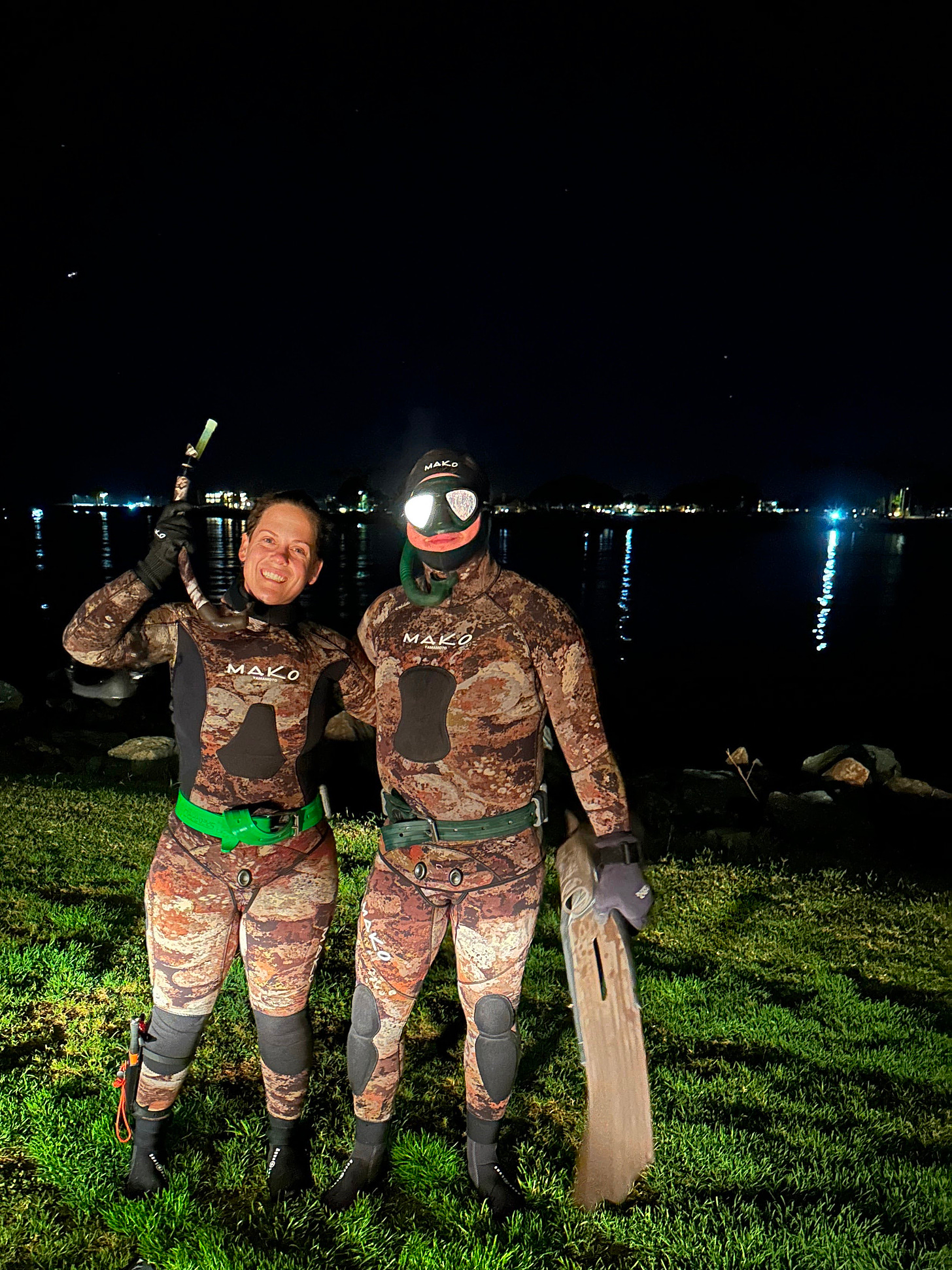 a man and woman in brown camouflage wetsuits at night by the water wearing masks and holding snorkels