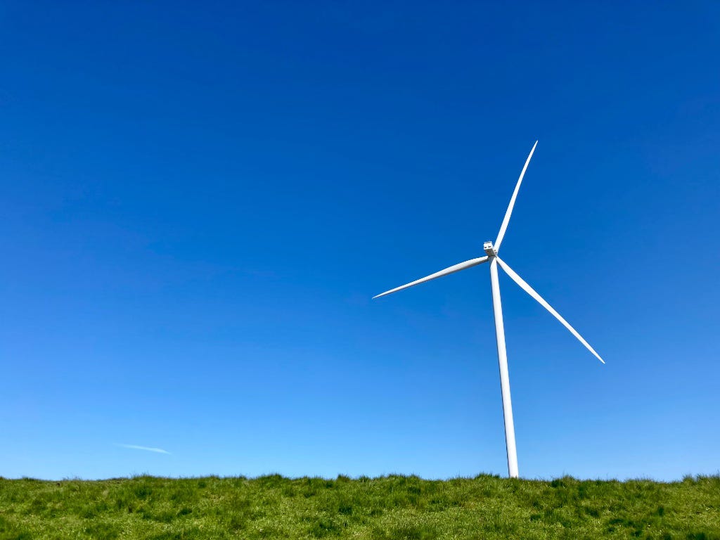 foto van een moderne windmolen met drie wieken die op een met gras bedekte dijk staat. Blauwheldere lucht op de achtergrond