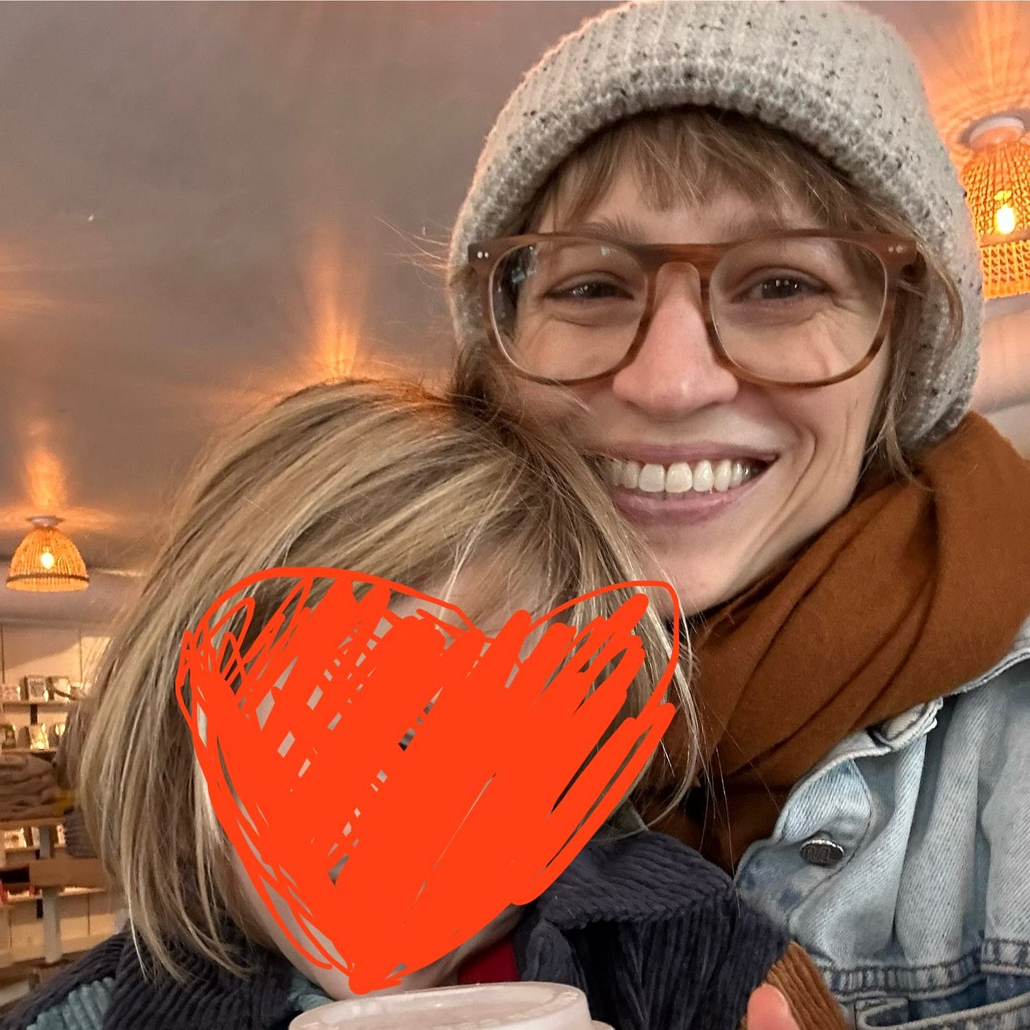 Sooz and her daughter smiling, with her daughter's face blurred out by a heart