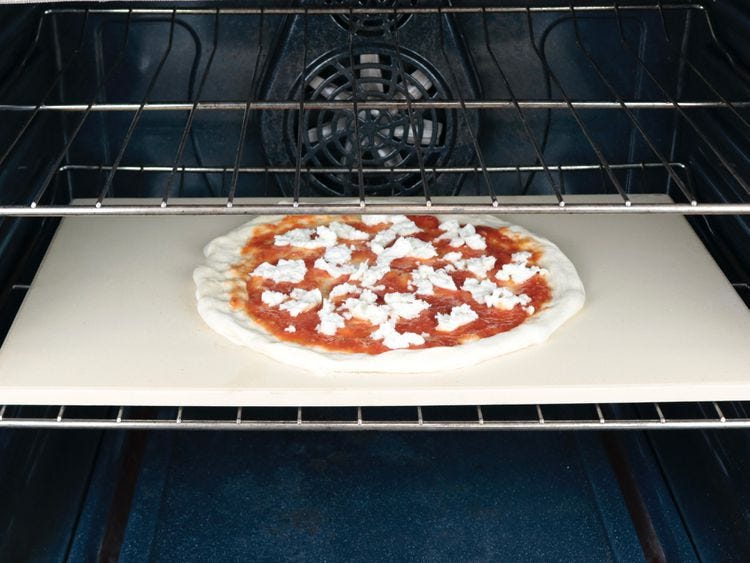 an uncooked pizza on a rectangular pizza stone on the bottom rack of an oven